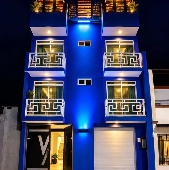 Fachada azul de LUMA iluminada de noche, con balcones blancos